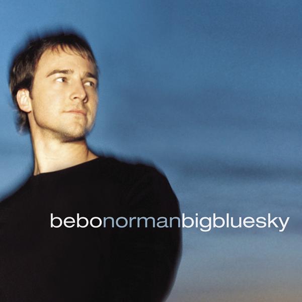 Album Art of Bebo Norman's Big Blue Sky album - A color photo of a young, white man in a black shirt being photographed from below him and off to the side. He's looking to the right of camera and has short, brown hair and a neutral expression. Behind him looks like a blue sky with a bit of darkness to it, so maybe a blue from dusklight or just before dawn. Printed over the photo is the artist's name above the shirt, and to the right of that is the album name with no spaces.
