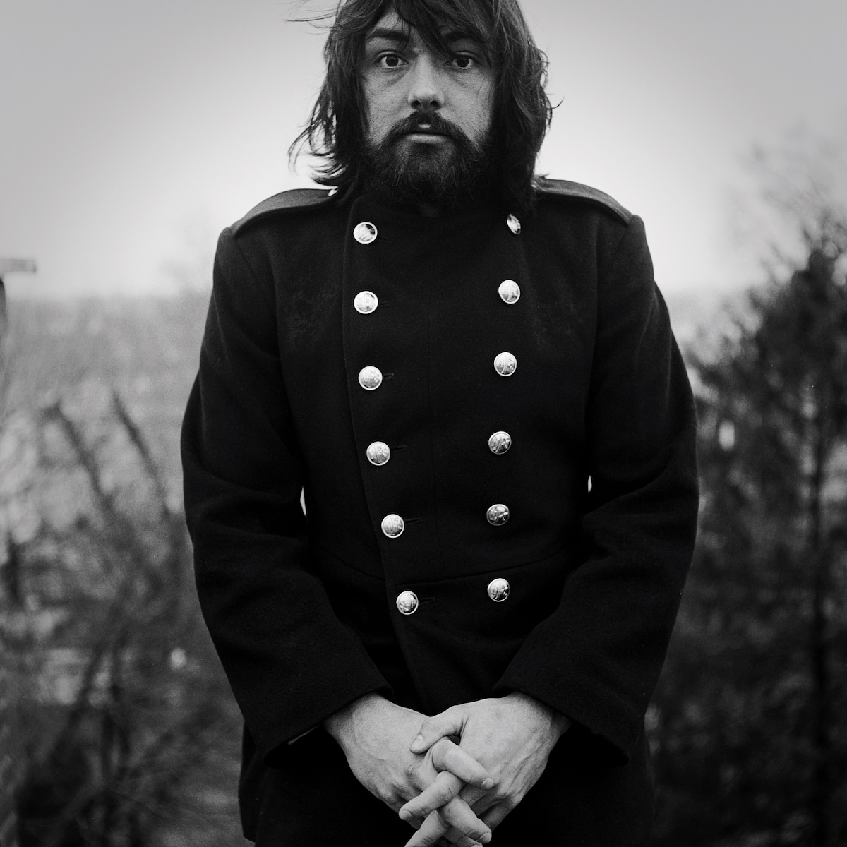 Album Art of Andrew Peterson's A Liturgy, A Legacy, and The Songs Of Rich Mullins album - A black-and-white photo of a man in a funny double-breasted coat that has large silver buttons on both the right and the left of the center. He's got a somewhat surprised look on his bearded face and has thick, dark hair. His hands are clasped together in front of his waist and and looks a bit awkward.</body></html>