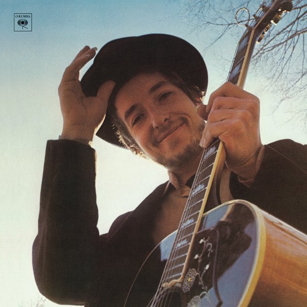Album Art of Bob Dylan's Nashville Skyline album - A photo of a young white man with a short beard and mustache in a black coat wearing a black hat, and he's holding his hand just below the hat like he's about to tip his hat. He has a noticeable smile and is photographed from below, looking down at the camera while holding his guitar in his left hand in front of him. Behind him can only be seen the blue sky, bluer towards the top and more white near the bottom.</body></html>