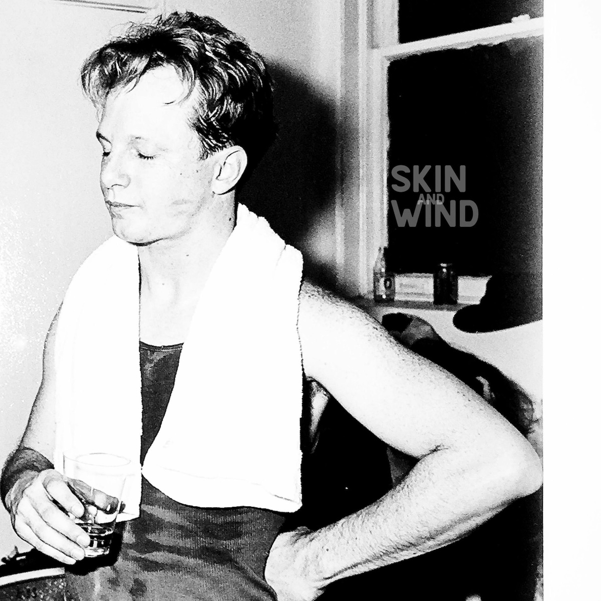 Album Art of Charlie Peacock's Skin And Wind album - A black-and-white photo of a young man standing with his eyes closed and a glass in his hand. His other hand is on his hip and his arms are bare, and it looks like he's been boxing or working out because he has a white towel around his neck. Behind him can be seen a window with a hat and a bottle and can of different drinks.</body></html>