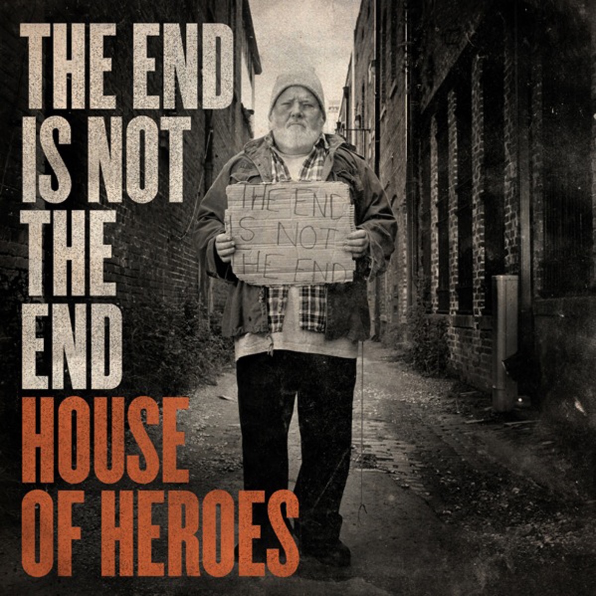 Album Art of House Of Heroes's The End Is Not The End album - In a narrow road between abandoned brick buildings, a black-and-white photo of a man with a white beard and a light-colored beanie is wearing a coat and a few more layers beneath it. In front of his chest he holds a piece of cardboard with the album title, 'The End Is Not The End', written on it in some sort of thin, black handwriting.</body></html>