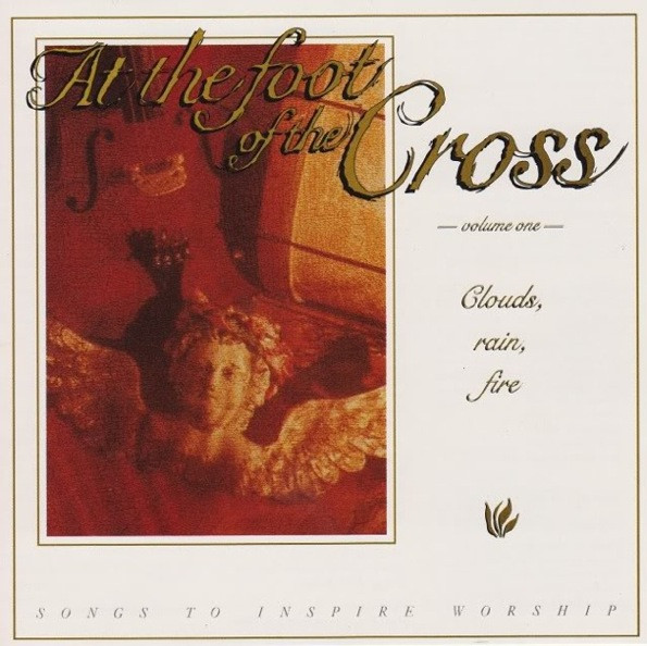  Clouds, Rain, Fire album - On a white background, a gold border is around the inside of the edges. At the top it has the text 'At The Foot' in large letters, with 'of the' below it in smaller and 'Cross' next to those words in even bigger gold script, all with a black drop shadow. In much smaller, to the right of a photo, it says 'volume one', and below that on the right is 'clouds', then below 'rain', and below 'fire'. On the left half behind the title and down is a photo of a bust of an angel sitting in on its side on a red background with a bunch of musical equipment like a drum and a violin can be seen as well. At the very bottom, in small black text, it says 'Songs To Inspire Worship'.