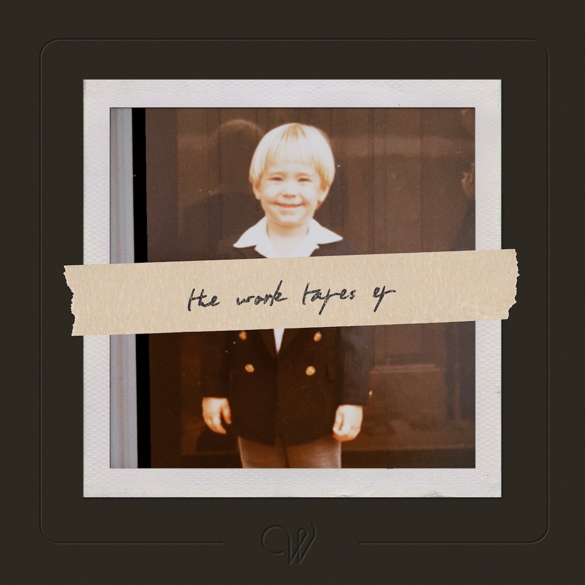 Album Art of Wilder Woods's The Work Tapes EP - A very large, thick black frame covers the edges, but it's so thick it covers about a quarter of the surface. In the middle, there's a photo of a chubby little kid with a white shirt and a small black suit coat over it with buttons down each side of the front. The kid has a big smile and blonde hair with a bit of a bowl cut look. It looks like he's photographed standing in front of a door. Around the edge of the photo is a small white matte edging. Above the whole photo and even extending into the frame is masking tape right across the middle horizontally, with 'the work tapes ep' handwritten on it in pen.